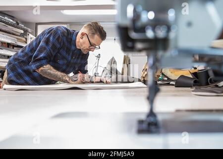 Presser foot and needle plate of shabby sewing machine on workbench on background of man working in upholstery workshop Stock Photo