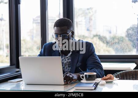 Serious African American male entrepreneur sitting at table in cafe and browsing netbook while working on project remotely Stock Photo