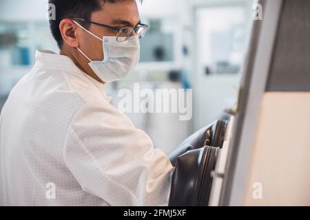 Side view crop concentrated male scientist in lab coat and mask holding hands in biosafety cabinet while working with contaminated materials Stock Photo