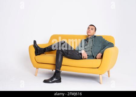 Young handsome male model in trendy clothes sitting on yellow couch on white background in studio Stock Photo