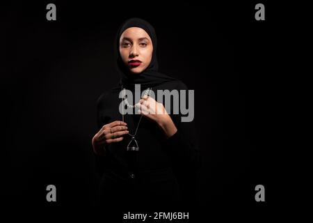 Attractive young Islamic female wearing black outfit and hijab gently looking at camera Stock Photo