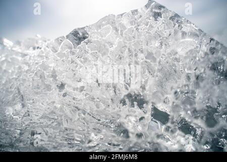 Transparent shining clear ice icicles close-up sparkling on frozen wild lake shore in sunset light. Cold winter nature background Stock Photo