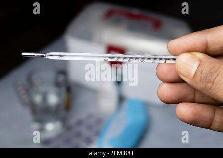 Selective focus on an analog thermometer held in human hand with medicine on background Stock Photo
