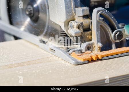 worker sawing wood board with electric circular saw. Carpenter working with a circular saw outside in sunny day. close-up Stock Photo
