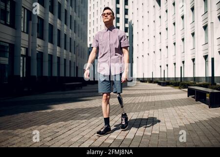 Disabled young man with leg prosthesis walking street. Stock Photo