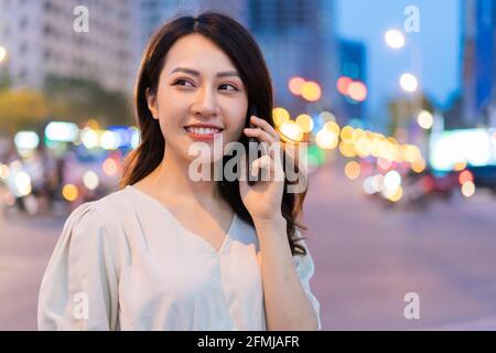 Young Asian woman calling while walking on the street at night Stock Photo