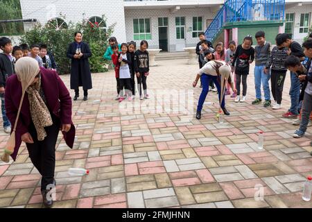 Teachers and students at the Lixian school of Hebei take part in the relay race to knock down the water bottles with the pantyhose on the head. Stock Photo