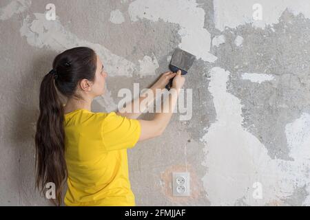A woman repairman puts a putty on the wall. Smearing the roughness. Repair with your own hands. Place for text Stock Photo