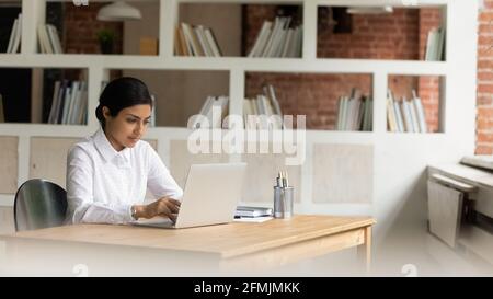 Confident Indian businesswoman working on laptop, sitting at desk Stock Photo