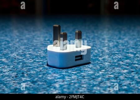 A 3 pin plug layed on it's back with a usb connector for charging phones layed on a mottled blue surface. Northampton, England, UK. Stock Photo