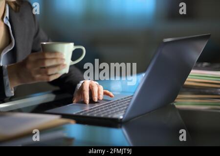 Close up of a businesswoman checking laptop content holding coffee cup in the night at office Stock Photo