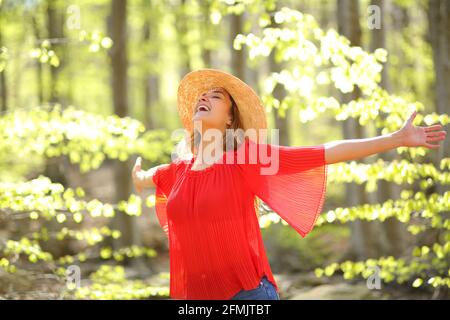 Excited woman spreading happiness outstretching arms in a green forest ...