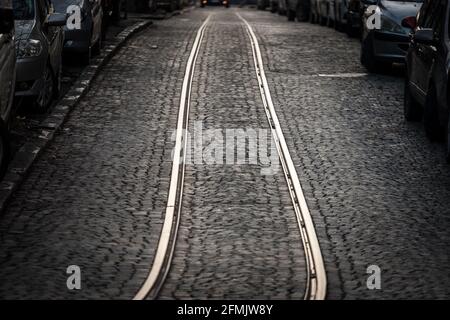 Picture of a tram track on a tramway on a cobblestone street of an urban downtown with cars parked around Stock Photo