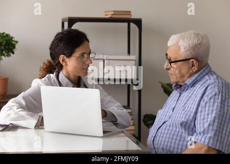 Young woman physician explain aged man therapy details using laptop Stock Photo