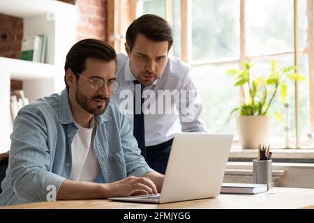 Two colleagues employees working on laptop together, using laptop Stock Photo
