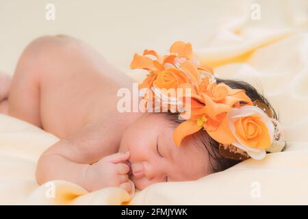 Portrait of a one month old sleeping, newborn baby girl. She is wearing a flower crown and sleeping on a cream blanket. Concept portrait studio fashio Stock Photo