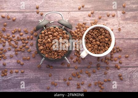 fresh coffee beans in a cup and alarm clock on table  Stock Photo