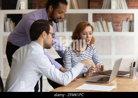 Three diverse colleagues working on project together, using laptop Stock Photo