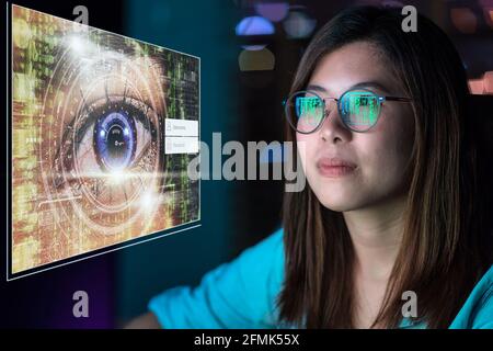 Portrait of Asia Businesswoman sitting and working hard via eye authentication with username and password over Closeup women eye with futuristic digit Stock Photo