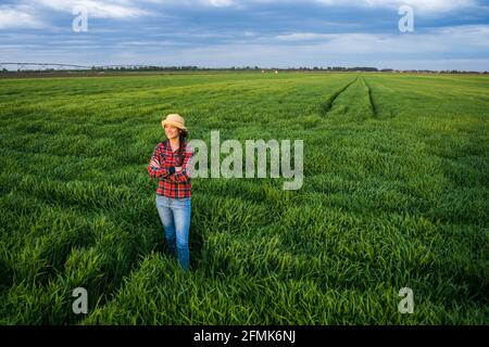 Proud female farmer is standing in her barley field and enjoying sunset. Stock Photo