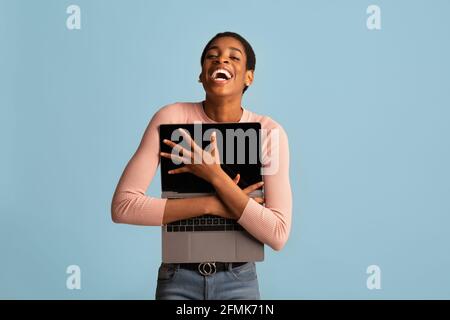 Online Shopping Lover. Cheerful Black Lady Embracing Opened Laptop And Laughing, Positive Young African American Woman Holding Computer While Posing O Stock Photo