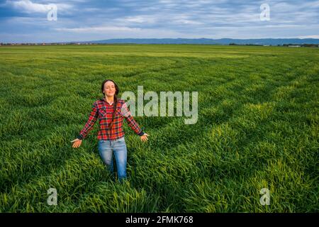Proud female farmer is standing in her barley field and enjoying sunset. Stock Photo
