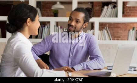 Smiling diverse colleagues chatting during break, sitting at desk Stock Photo