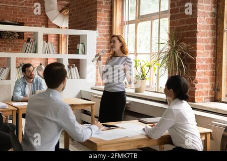 Confident businesswoman holding microphone, leading briefing with diverse employees Stock Photo