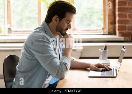 Side view thoughtful businessman in glasses looking at laptop screen Stock Photo