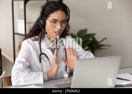 Confident female therapist in headphones consult patient by video call Stock Photo