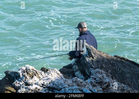A mature man fishing from rocks at Towan Head in Newquay in Cornwall. Stock Photo