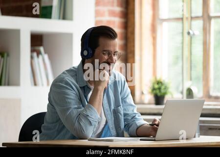 Smiling man in glasses and headphones looking at laptop screen Stock Photo