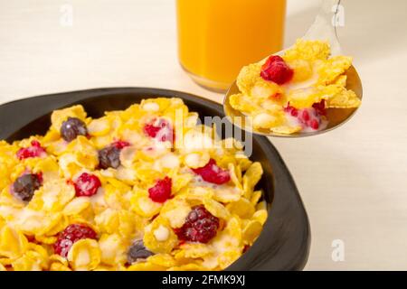 Healthy breakfast Cornflakes with raspberry, blueberry and milk in black wooden bowl and on a spoon for breakfast Stock Photo