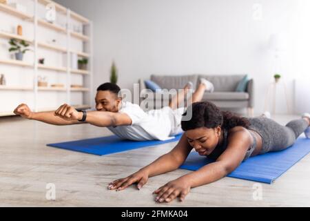 Young black woman feeling tired during yoga practice with her boyfriend at home. Millennial African American couple exercising on yoga mats, having in Stock Photo
