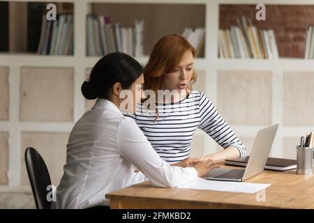 Two diverse businesswomen working on project together, using laptop Stock Photo