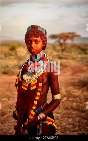 A young Hamar girl, with colorful necklaces, bracelets and an apron made of goatskin from the village Gabo in the light of the setting sun. 16.02.2007 Stock Photo