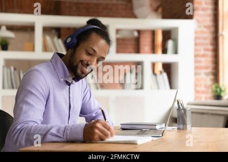 Smiling African American man in headphones taking notes, studying online Stock Photo