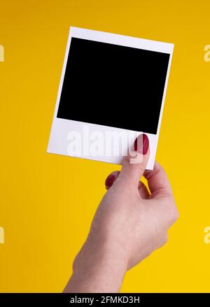 woman hand holding picture frame instant pack polaroid film  with space card on yellow background Stock Photo