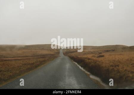 Looking through a car windscreen out onto a mountain road going across bleak moorland on a wet stormy day. With rain drops  on the window. Stock Photo