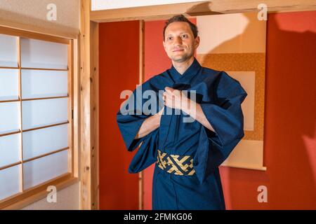 Traditional japanese machiya house room with sliding door window and red alcove with hanging scroll and happy man in blue kimono smiling at tea ceremo Stock Photo