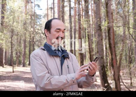 Half-length portrait of senior Asian man using mobile phone in forest park. Stock Photo