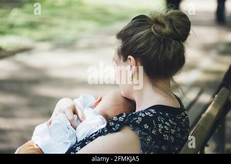 mother holding her baby in her arms on bench in park on a sunny summer day Stock Photo