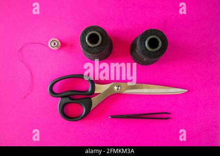Black tailoring accessories as scissors, thread, tweezers and bobbin on pink background Stock Photo