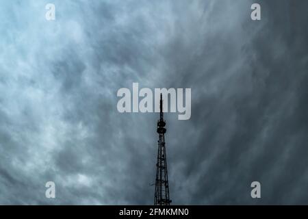 A television or radio broadcasting antenna against a dramatic overcast sky.A cloudy sky with thick rain clouds and a telephone antenna.Communications Stock Photo