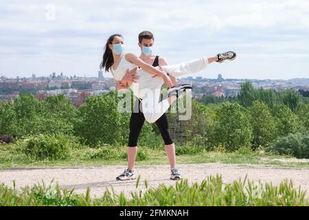 Young couple practicing street dance, ballet, dancing steps, movements at a park wearing protective face masks. Stock Photo