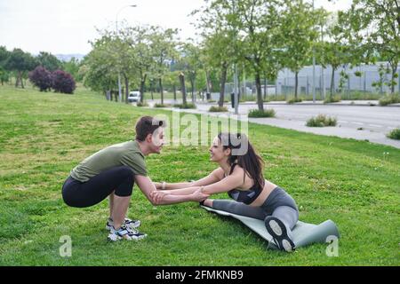 Personal trainer helping young woman doing splits and stretching exercises during fitness workout in a park. Exercise outside. Stock Photo