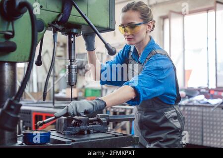 Woman worker in metal workshop greasing drill Stock Photo