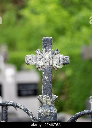 Weathered and old iron cross on a fence near a cemetery Stock Photo