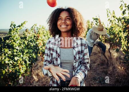Mixed race female farmer playing with vegetables standing in vineyard  Stock Photo