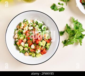 Close up view of avocado, prawn, tomato and mozarella salad with greens in bowl over light stone background. Healthy diet food concept. Top view, flat Stock Photo